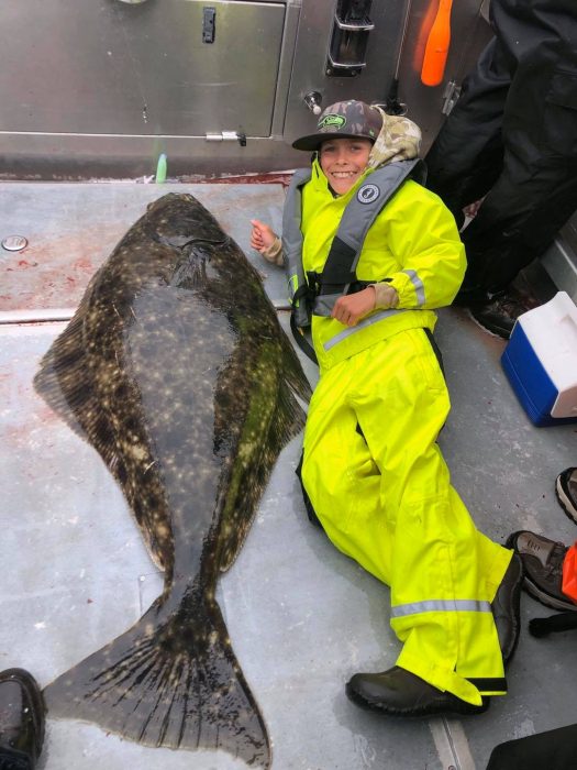 child lays on deck of Silver Streak boat posing with trophy halibut caught self-guided sport fishing