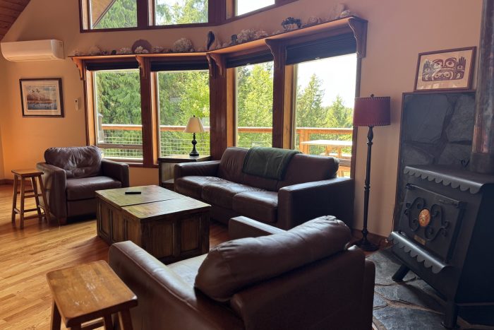 living room of an authentic alaskan cabin at a ketchikan fishing lodge showing large windows overlooking deck, leather furniture and wood stove