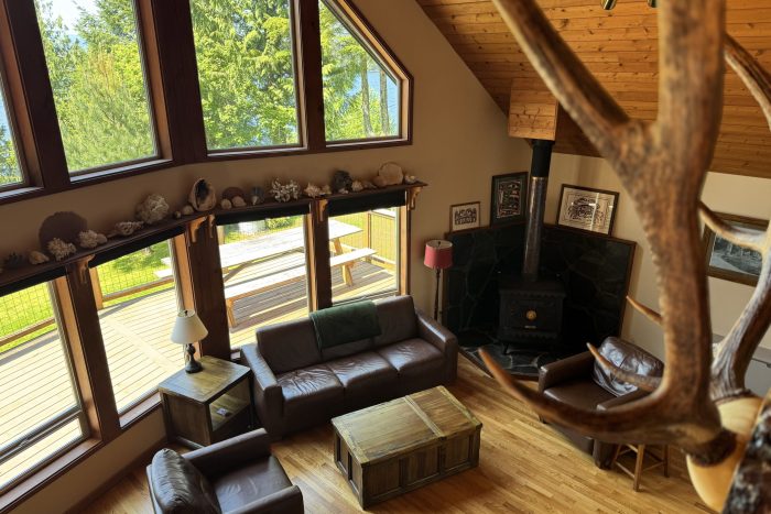 View from the loft of the Alder House cabin at Chinook Shores lodge showing off the authentic Alaskan decor, ample living area, leather furniture, wood stove in the living room, and sweeping views of the water and trees
